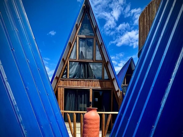 A triangular building with a wooden facade and large windows, surrounded by blue structures. - Pousada Quilombo do Tibau (Tibau)