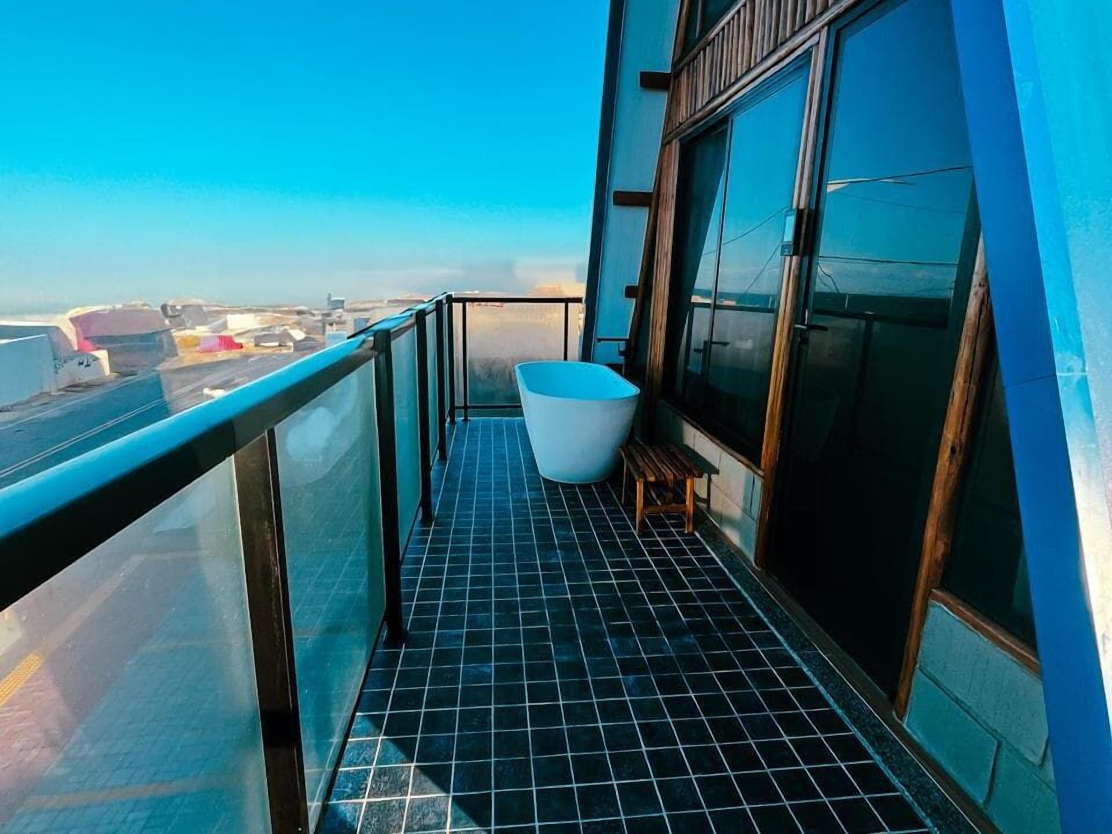 A balcony with a bathtub, a wooden bench, and a view of the airport.