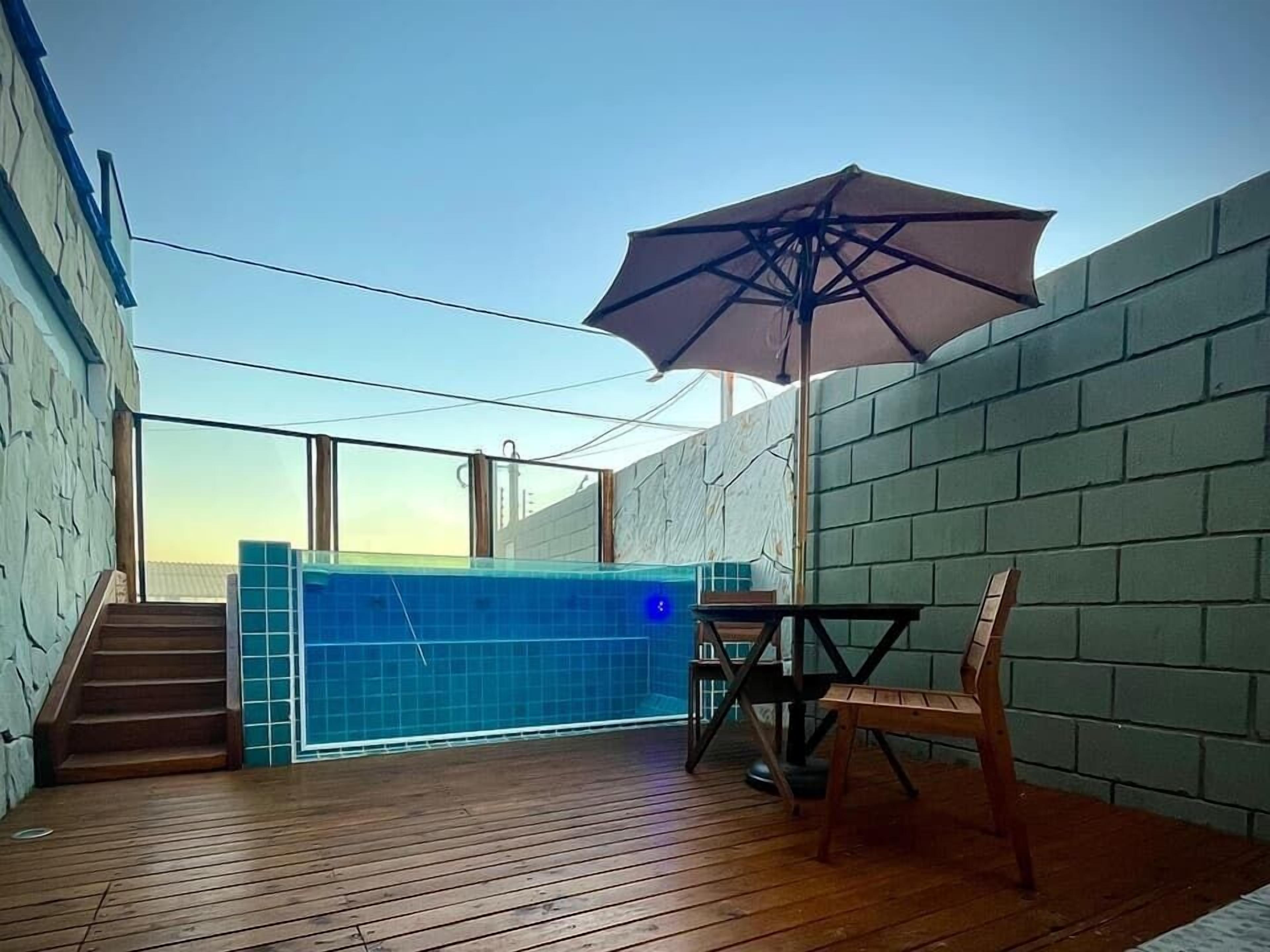 A rooftop pool area with a wooden deck, a large umbrella, and a view of the city skyline.