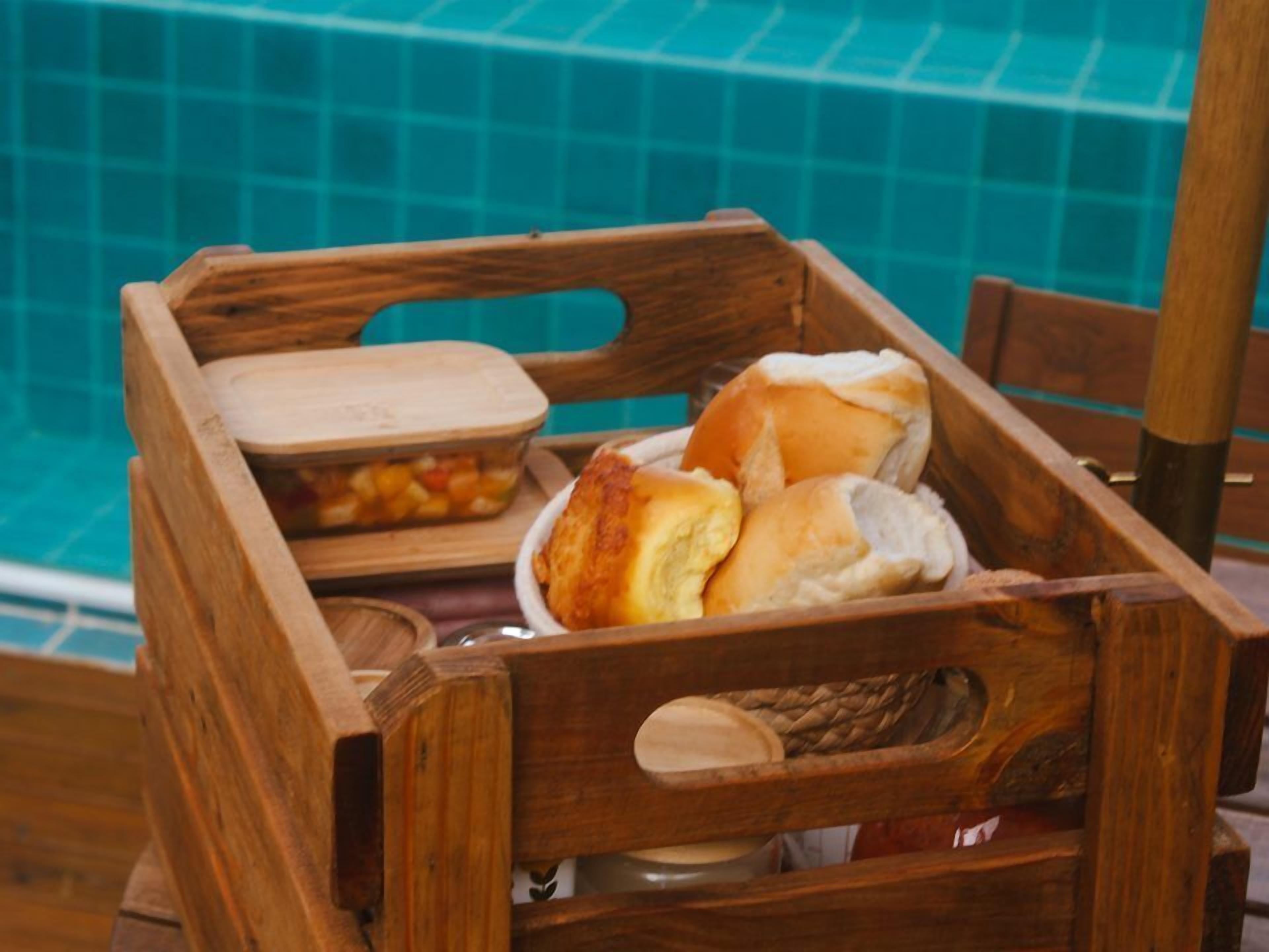 Una caja de madera con una bandeja de madera que contiene pan y un recipiente con fruta.