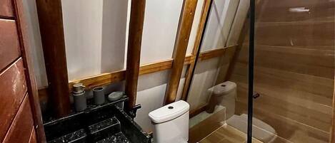 A small bathroom with a toilet, a shower enclosure, and a sink with a black countertop.