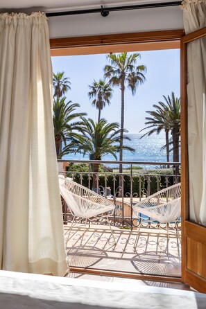 A balcony with a view of palm trees and the sea, a white chair, and a hammock. - Casa Sembat with sea views, pool and Wi-Fi (Cala Millor)