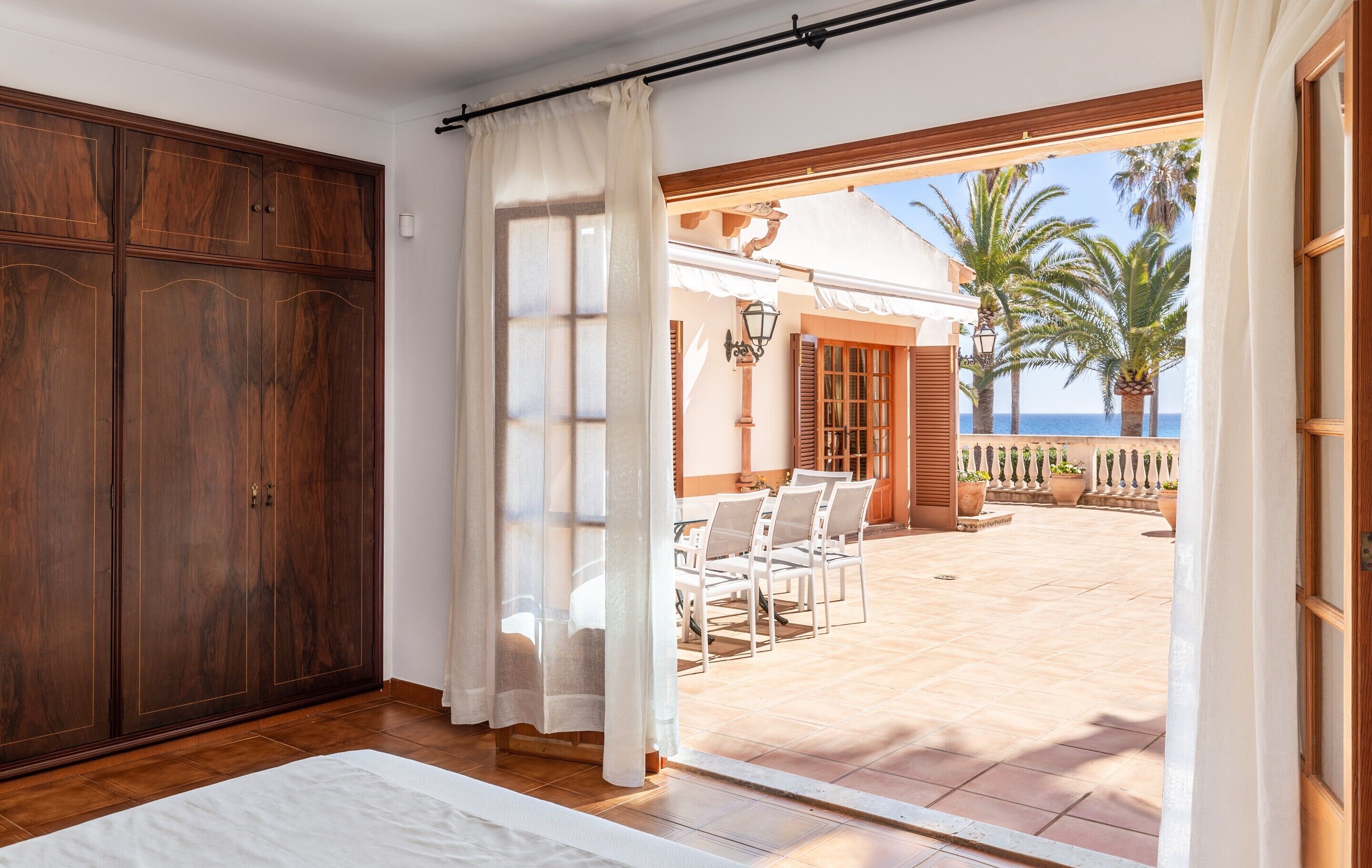 Una habitación con un armario de madera, una cama blanca y vistas a un patio exterior con mesa y sillas.