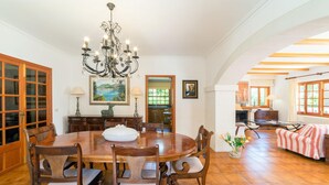 Une salle à manger avec une table en bois, des chaises, un lustre et une vue sur la cuisine.