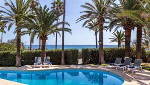Une piscine avec des chaises longues, des palmiers et une vue sur la mer.
