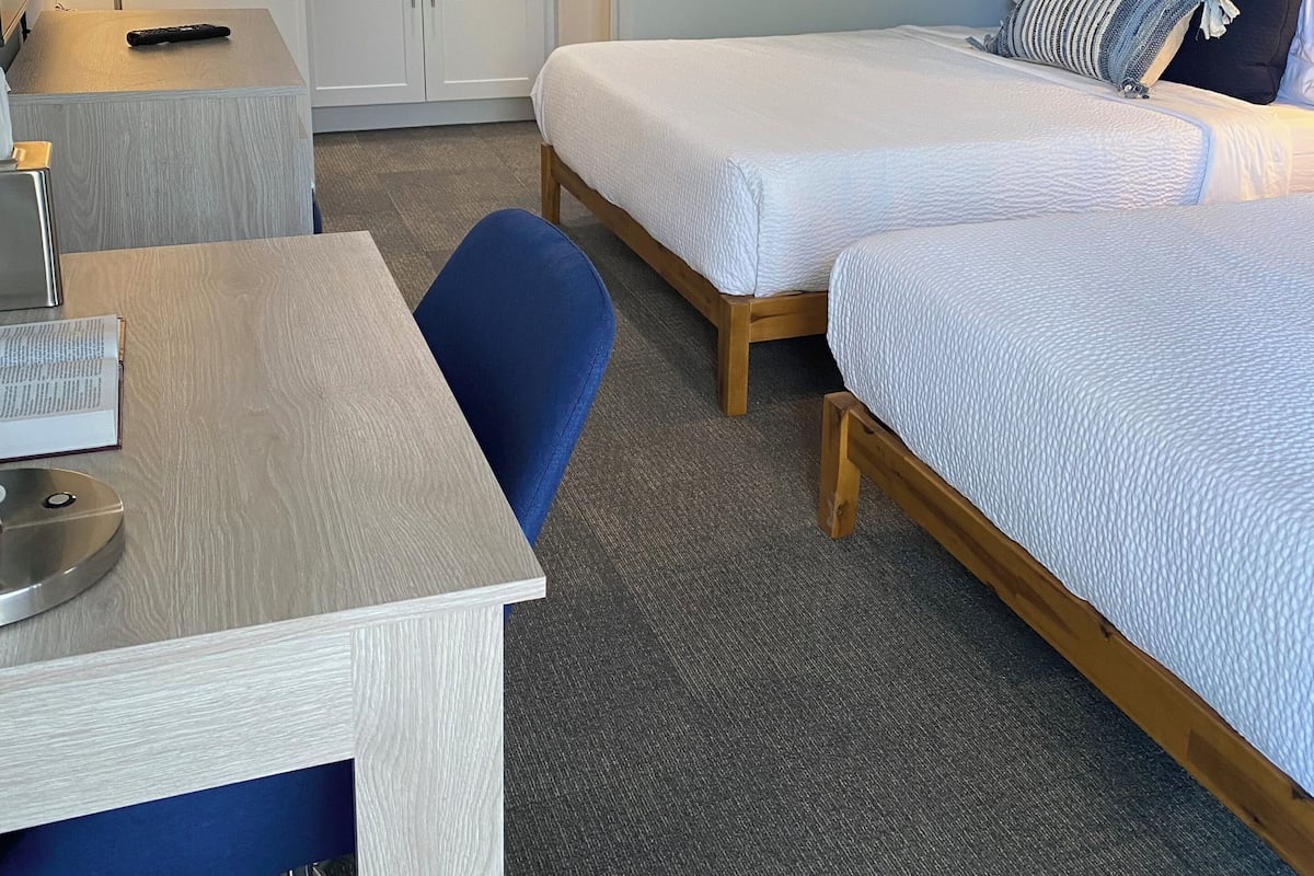 A hotel room with a desk, two beds, a mirror, and a blue accent wall.