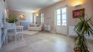 A spacious room with a white sofa, a dining table with chairs, a potted plant, and a radiator.