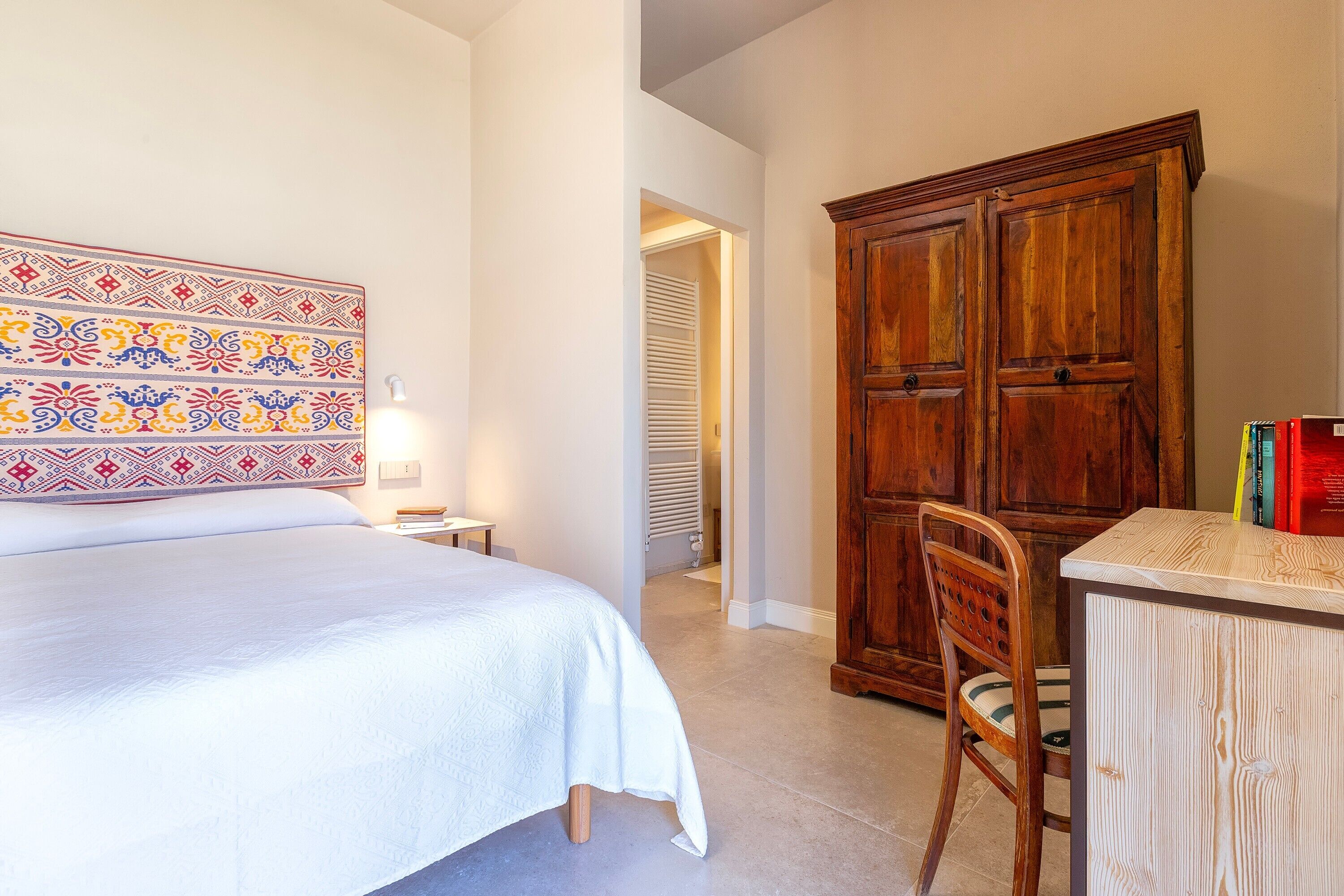 A bedroom with a bed, a wooden cabinet, a chair, and a patterned headboard.