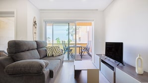 A modern living room with a grey sofa, a flat-screen TV, and a large sliding glass door leading to an outdoor area. - The Pine Flat with Pool at Furadouro (Ovar)