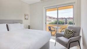 Une chambre d’hôtel avec un grand lit, une chaise et un balcon donnant sur des immeubles.