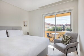 A hotel room with a large bed, a chair, and a balcony with a view of buildings.