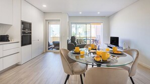 Une cuisine moderne avec des meubles blancs, une table à manger en verre et un coin salon comprenant un canapé et des fauteuils.