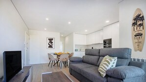 Un salon moderne avec un canapé gris, un téléviseur à écran plat et un coin repas comprenant une table et des chaises.