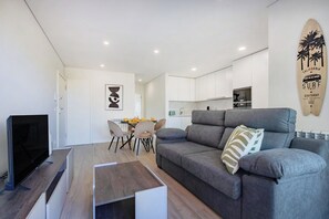 A modern living room with a grey sofa, a flat-screen TV, and a dining area with a table and chairs.