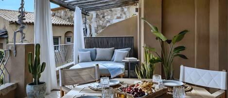 A terrace with a dining table set for two, a potted cactus, and a cushioned seating area.