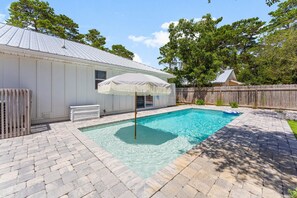 En baghave med swimmingpool, en overdækket terrasse og et træhegn.
