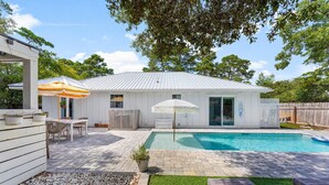 A backyard with a swimming pool, a patio with a table and chairs, and a covered seating area. - Cottage Haven (Santa Rosa Beach)