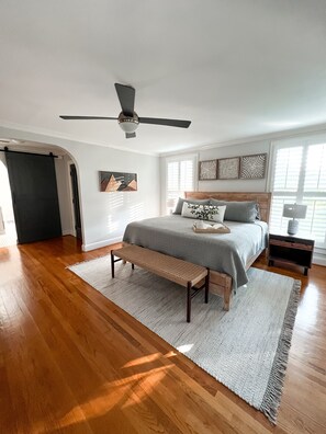 Une chambre à coucher avec un lit, un banc, un ventilateur de plafond et des œuvres d’art accrochées aux murs.