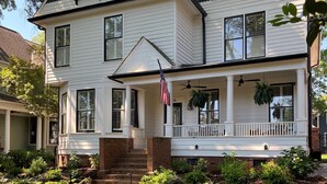 Een tweelaags huis met een veranda, een vlag en een verzorgd gazon.
