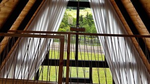 A triangular attic room with wooden beams and a large window with white curtains.