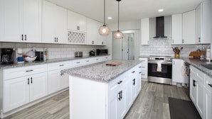 A modern kitchen with white cabinets, granite countertops, a central island, stainless steel appliances, and pendant lighting. - Cozy Corner: Spacious Area & Outdoor Lounges! (Knoxville)