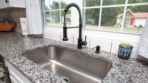 A kitchen with a granite countertop, stainless steel sink, and a window with a view of houses. - Cozy Corner: Spacious Area & Outdoor Lounges! (Knoxville)