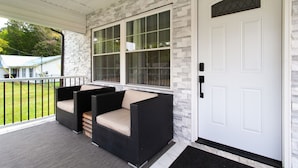 A porch with wicker furniture and a white door. - Cozy Corner: Spacious Area & Outdoor Lounges! (Knoxville)