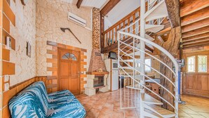 Ein großzügiger Wohnbereich mit Steinsäule, Holztreppe, einer Couch und einem Kamin.