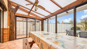 Eine überdachte Terrasse mit Tisch und Stühlen, einem Deckenventilator und Blick ins Freie.