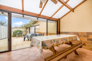A patio with a table covered by a tablecloth, wooden benches, and a view of the backyard.