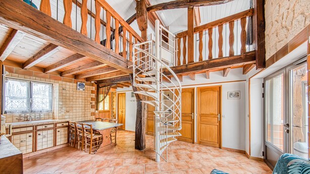Eine geräumige Küche mit Kochinsel, Holzbalken und einer Wendeltreppe.