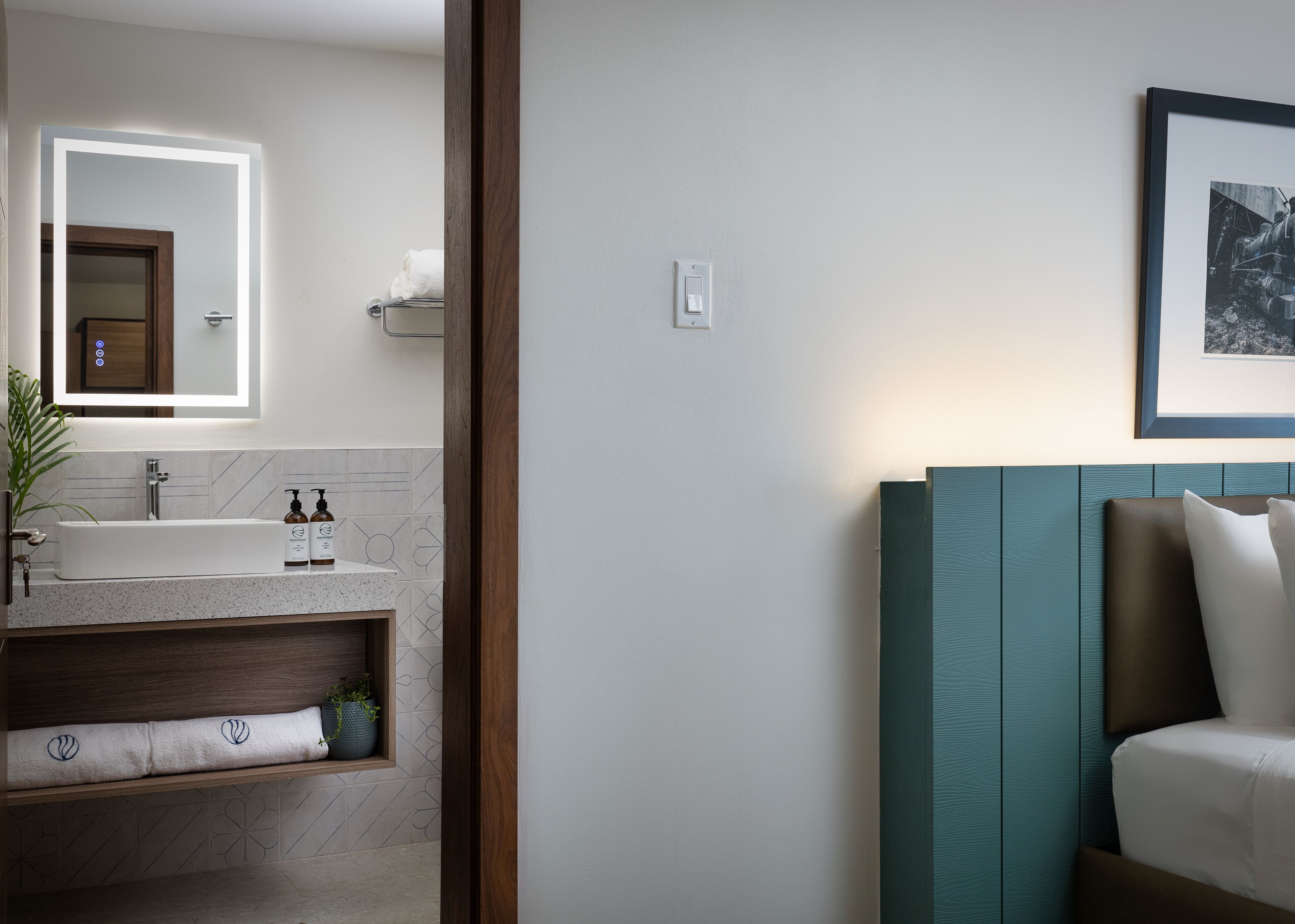 A modern bathroom with a large mirror, a sink, and a vanity. There is a framed picture on the wall and a plant on the vanity.