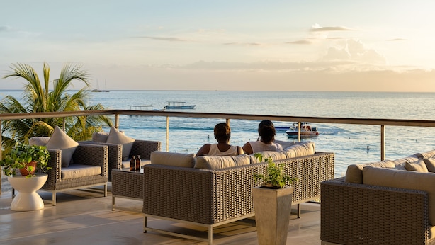 A terrace with wicker furniture and potted plants, overlooking a calm sea and boats. - Negril Footeprints Hotel (Negril)