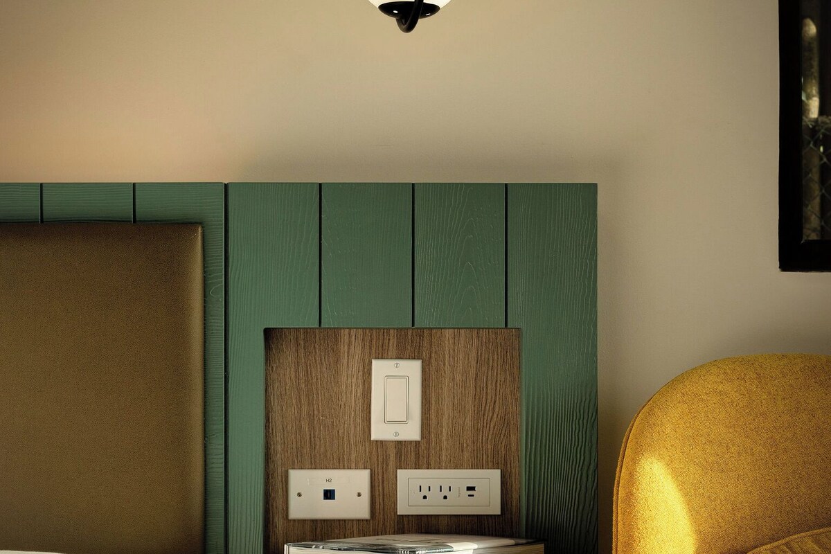 A modern hotel room with a bed, a nightstand with a lamp, and a green wall panel.