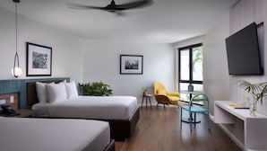 A hotel room with two beds, a ceiling fan, a TV, a small table with a chair, and framed pictures on the walls. - Negril Footeprints Hotel (Negril)
