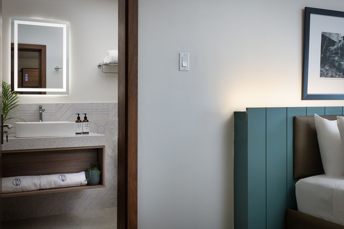 A modern bathroom with a large mirror, a sink, and a vanity. There is a framed picture on the wall and a plant on the vanity.