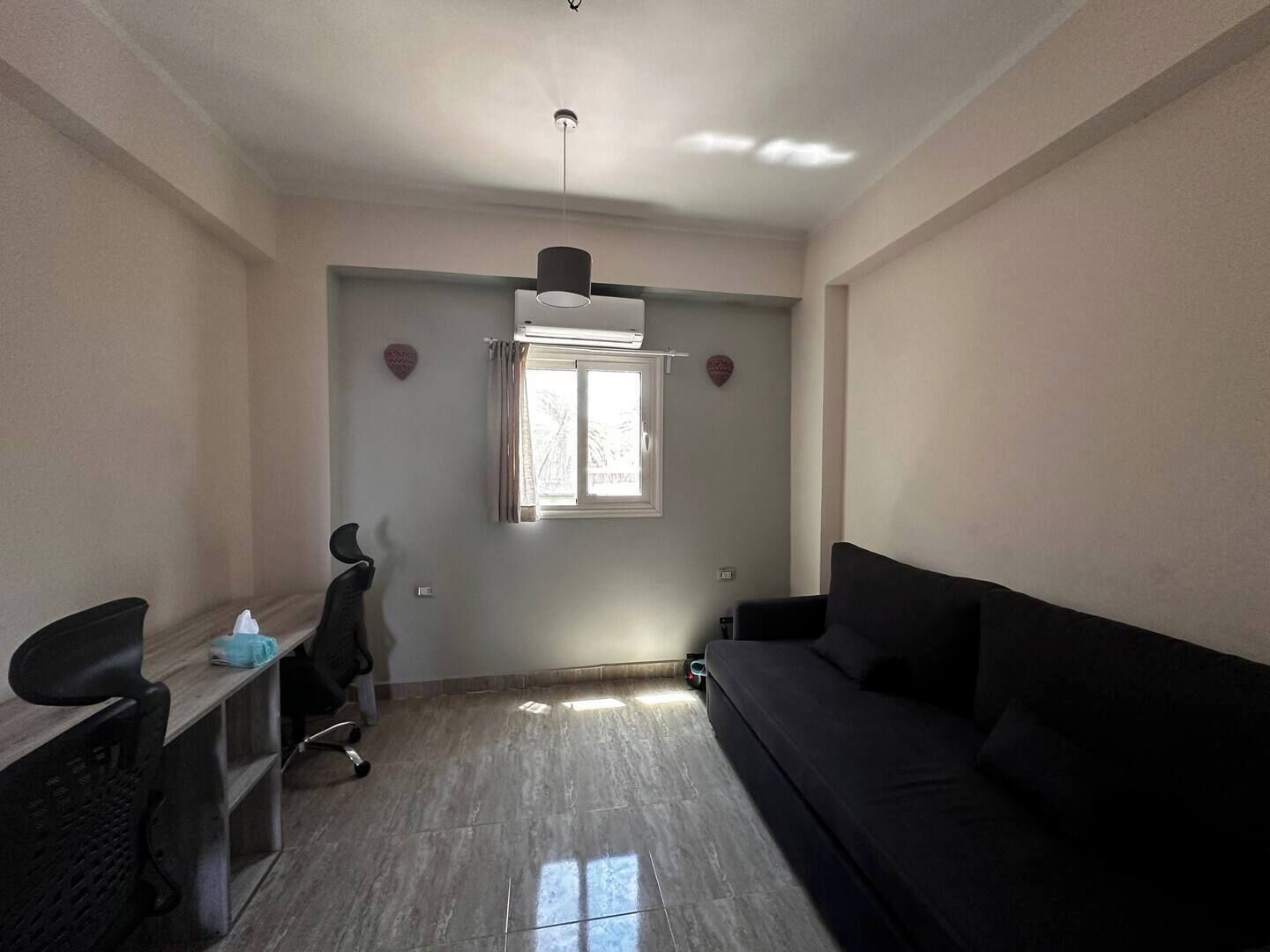 Um quarto com escrivaninha, poltrona, sofá, janela e ventoinha no teto.
