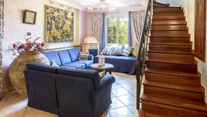 A living room with a blue sofa, a large vase with flowers, a wooden staircase, and a painting on the wall. - VILLA LISA - COUNTRY HOUSE LISA. HOUSE WITH GARDEN 7 MINUTES WALK FROM THE SEA (Diano Marina)
