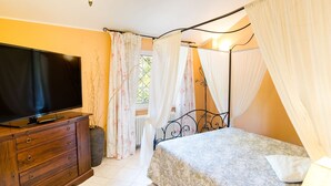 A bedroom with a bed, a TV on a wooden dresser, and a window with curtains. - VILLA LISA - COUNTRY HOUSE LISA. HOUSE WITH GARDEN 7 MINUTES WALK FROM THE SEA (Diano Marina)