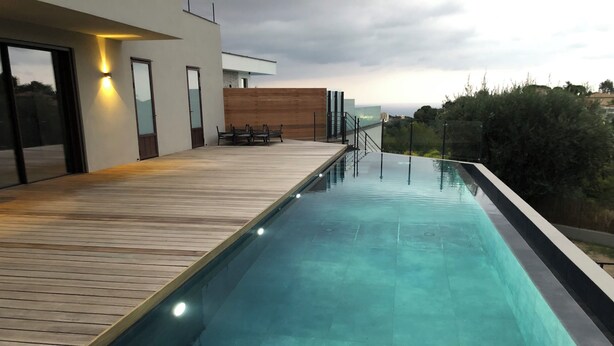 A modern outdoor swimming pool with a wooden deck, surrounded by a wooden fence and a glass wall. - CONTEMPORARY VILLA 350 m2 SEA VIEW SWIMMING POOL (Nice)