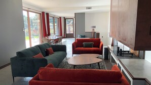 A modern living room with a green sofa, red armchairs, and a coffee table. There is a dining area with a table and chairs visible through large windows. - CONTEMPORARY VILLA 350 m2 SEA VIEW SWIMMING POOL (Nice)