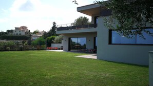 A modern building with a flat roof, large glass windows, and a spacious outdoor area with a lawn and seating. - CONTEMPORARY VILLA 350 m2 SEA VIEW SWIMMING POOL (Nice)