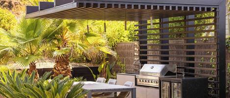 An outdoor patio with a grill, seating, and a pergola structure.