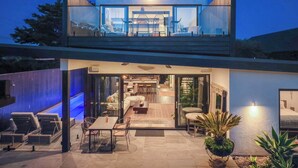 Une maison moderne à deux étages, dotée d’un balcon en verre, d’un espace extérieur aménagé pour se détendre et d’un intérieur bien éclairé.