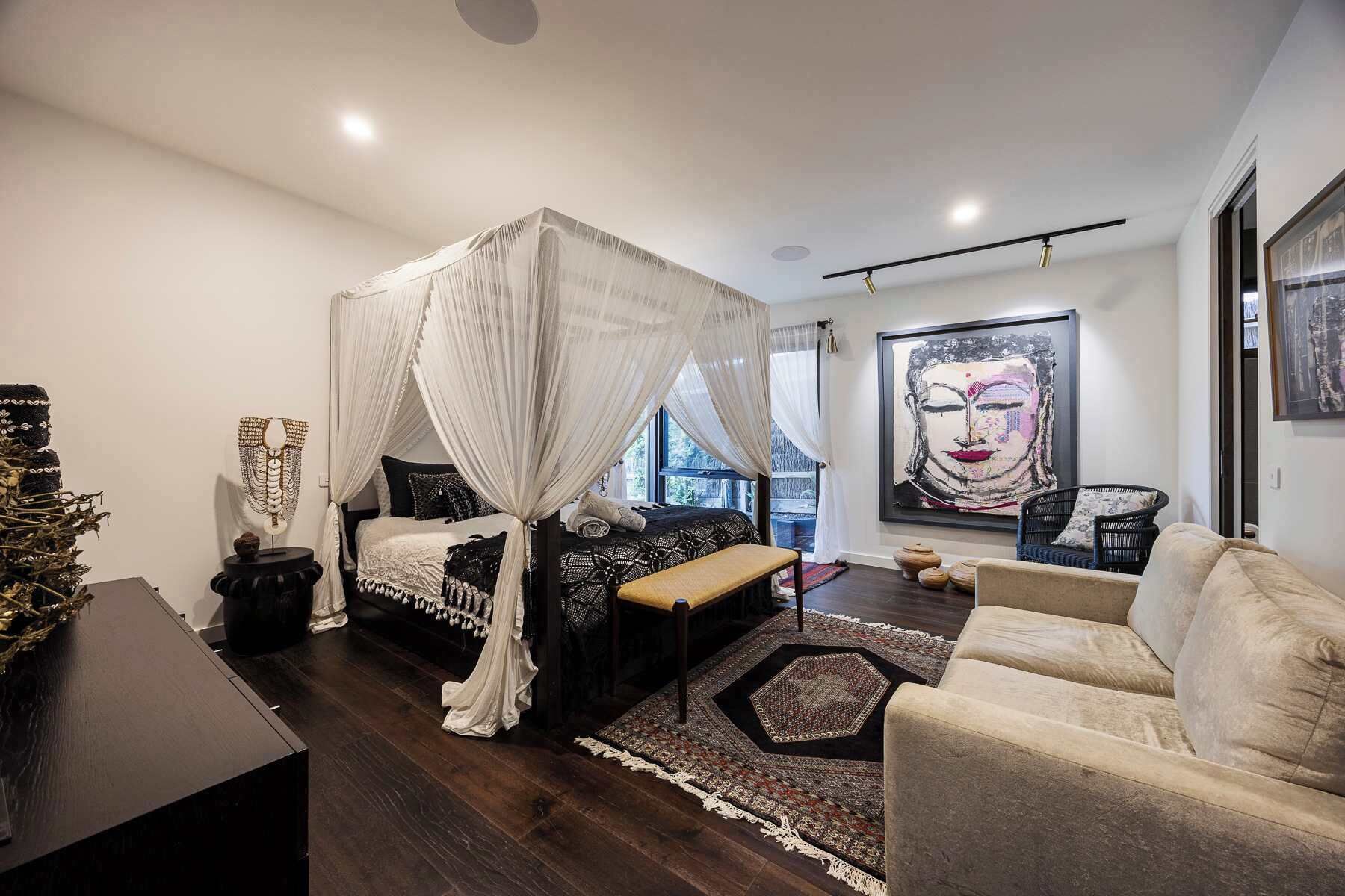 A modern bedroom with a canopy bed, a large artwork on the wall, and a view of the outdoors.
