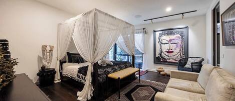 A modern bedroom with a canopy bed, a large artwork on the wall, and a view of the outdoors.