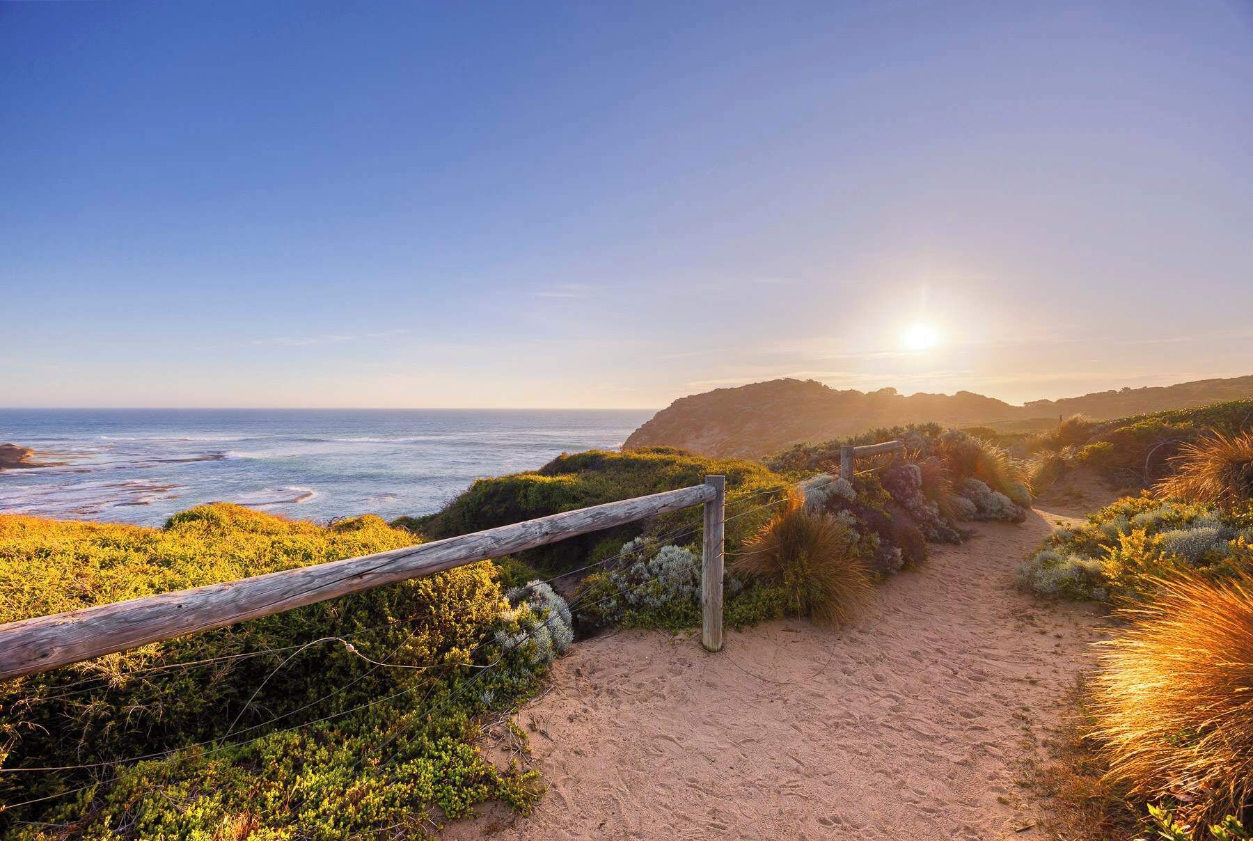 A coastal path with a wooden fence, leading to a beach with ocean views.