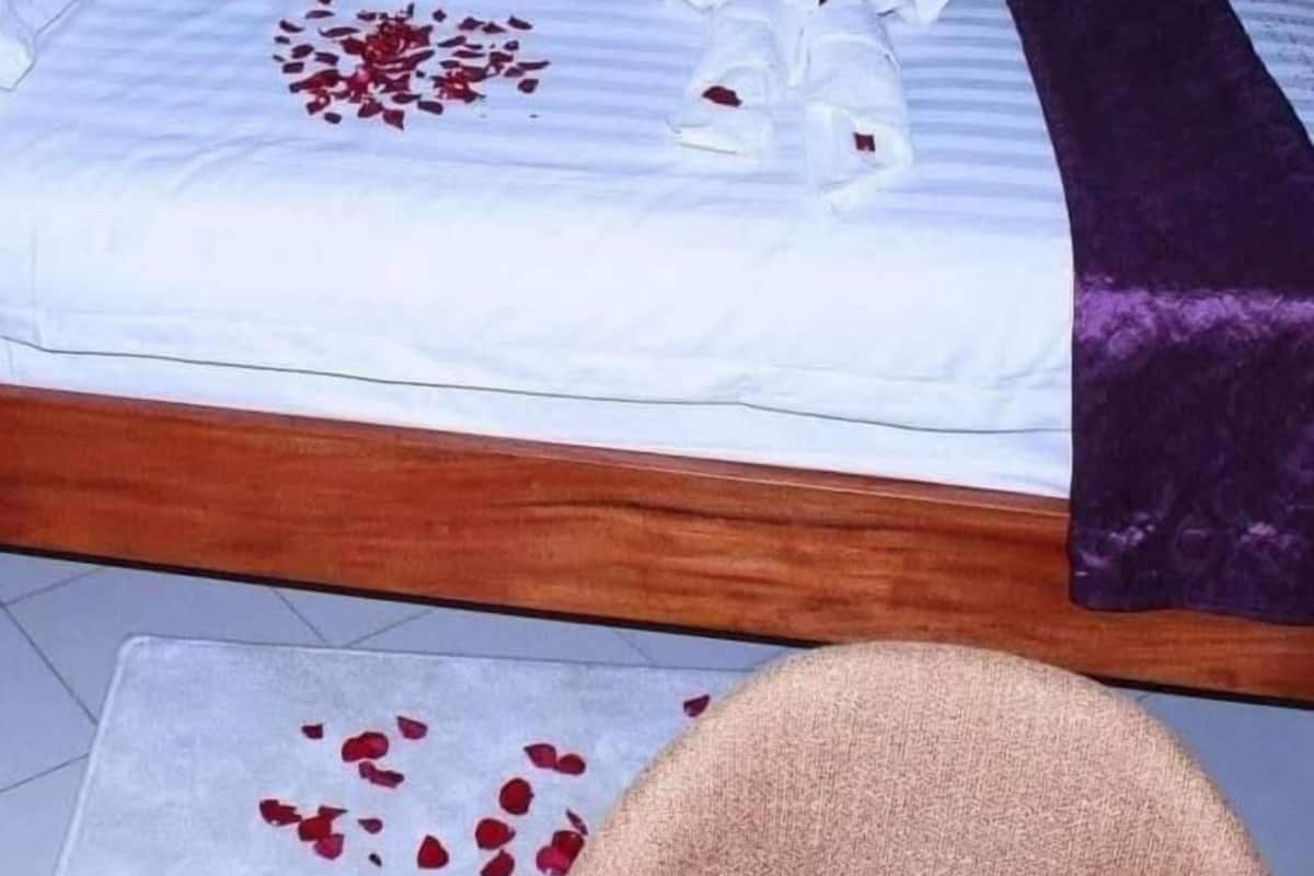 A neatly made bed with white linens, a purple throw blanket, and scattered rose petals.