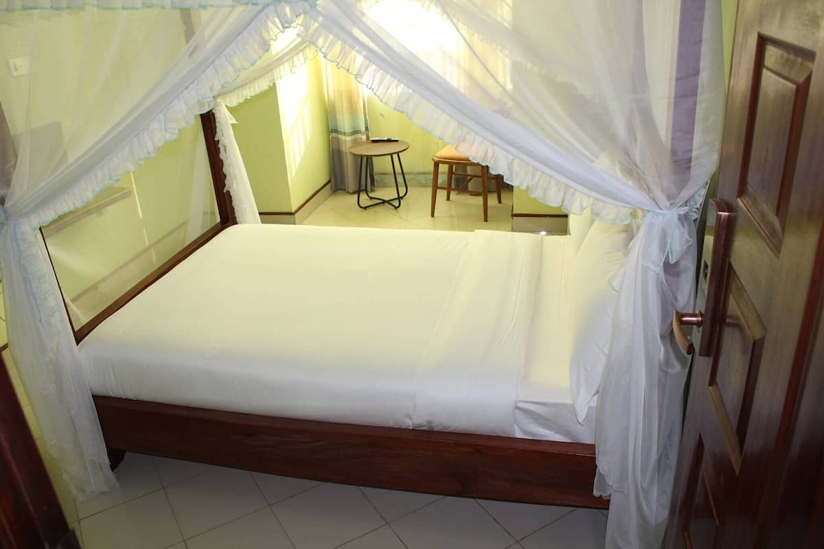 A bed with a canopy, a small round table, and a chair in a room with a door and a window.