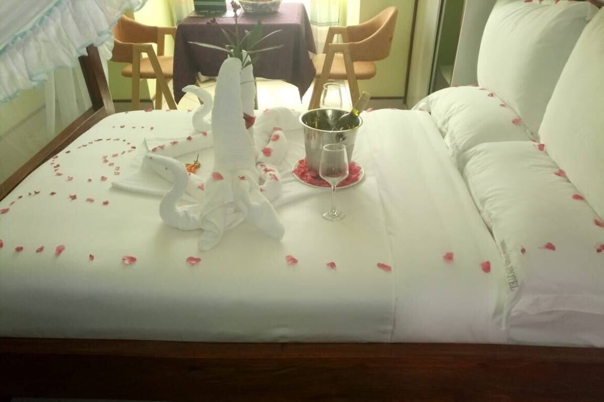 A bed with a white bedspread, two swan-shaped pillows, a champagne bottle, and a wine glass.